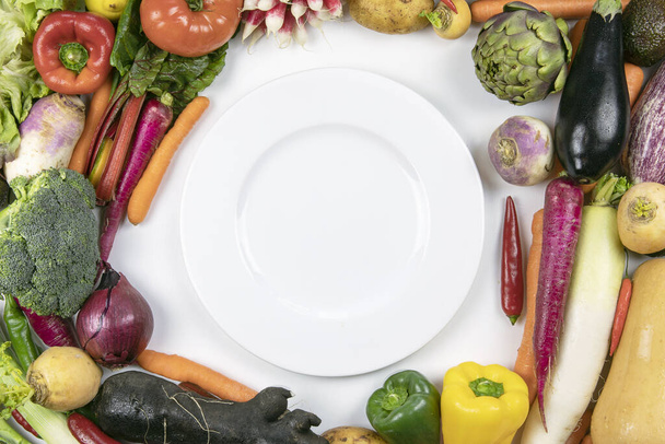 A lot of colorful fresh vegetable flat lay frame with round white plate inside. Healthy diet. - Photo, Image