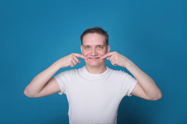 stílusos portré egy vicces jóképű fiatal srác fehér pólóban kiváló hangulatban fényes kék háttér - Fotó, kép