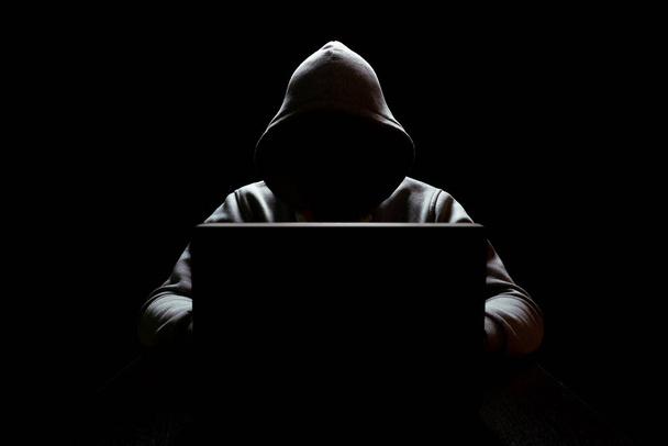cybercrimp with a hidden face in the dark in front of a laptop, network security - Fotoğraf, Görsel