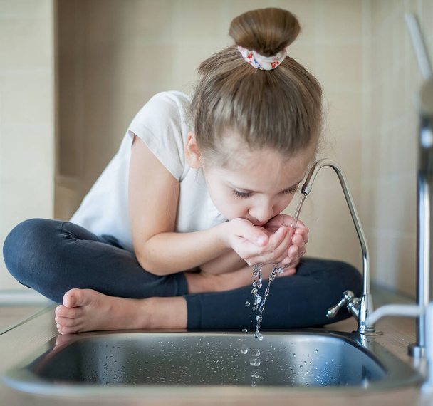 Caucasian little girl drinking from water tap or faucet - Foto, afbeelding