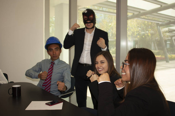 Mujeres y escuchar a miembros del equipo empoderados con puños en alto por su jefe que lleva una máscara de luchador mexicano para motivarlos
 - Foto, imagen