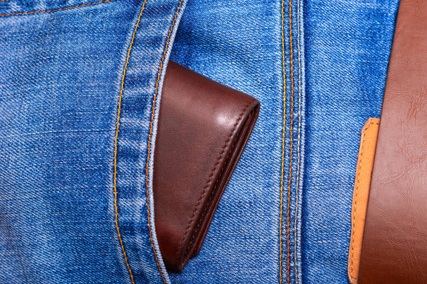 Kahverengi deri cüzdanın, kot pantolonun arkasından süzülüyor. - Fotoğraf, Görsel