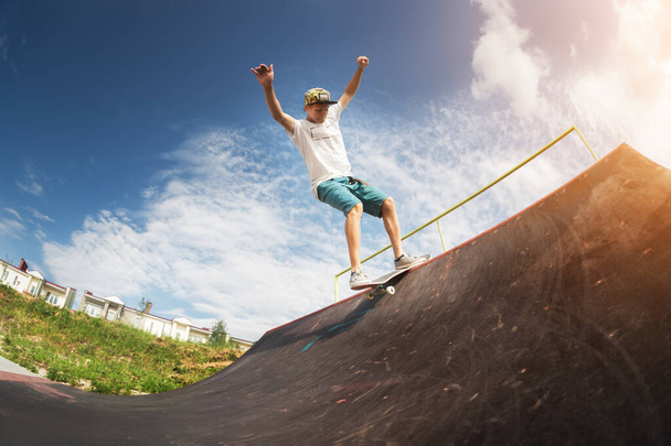 Portrait of a young skateboarder doing a trick on his skateboard on a halfpipe ramp in a skate park in the summer on a sunny day. The concept of youth culture of leisure and sports - Foto, Imagen