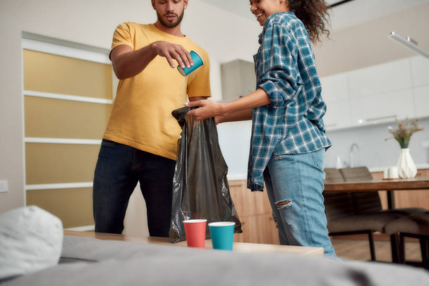 Clean and healthy house. Young multicultural couple in casual clothes sorting garbage and smiling while cleaning their modern kitchen together - Foto, Imagen