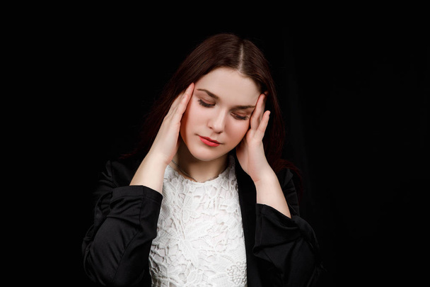 Portrait of beautiful young brunette wore a black jacket touching her temples, the feeling of stress, the feeling a headache, on black background - Fotografie, Obrázek