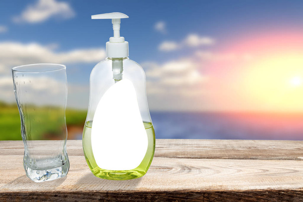 Glass cup with dishwashing detergent stand against the backdrop of nature. - Φωτογραφία, εικόνα