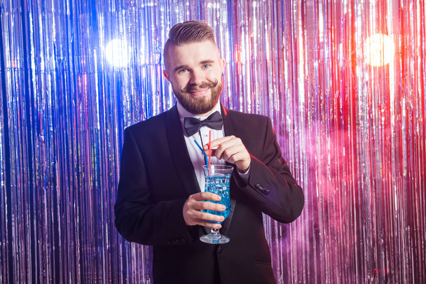 Club party and holidays concept - Portrait of elegant handsome man in a expensive suit holds blue cocktail on shiny background. - Фото, изображение