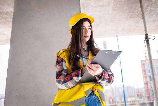 Гарненька жінка-працівник оглядає робочий процес на будівельному майданчику, заповнює документи
 - Фото, зображення