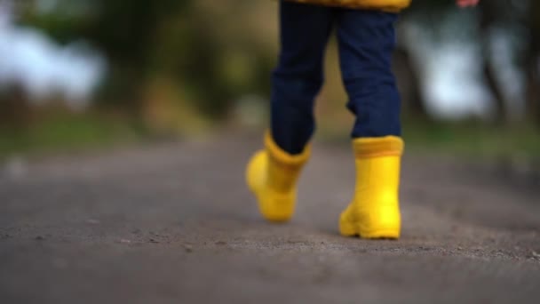 Boldog gyermeklábak sárga gumicsizmában az úton sétálva ősszel - Felvétel, videó