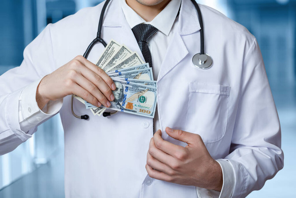 Doctor hides a money bribe in a side pocket . - Фото, изображение
