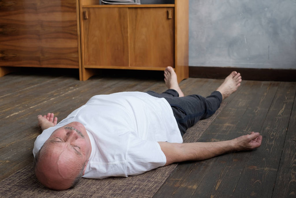 Yoga. Senior man meditating on a wooden floor and lying in Shavasana pose. - Valokuva, kuva