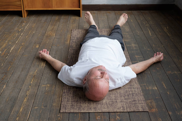 Jóga. Starší muž meditující na dřevěné podlaze a ležící v Shavasana póze. - Fotografie, Obrázek