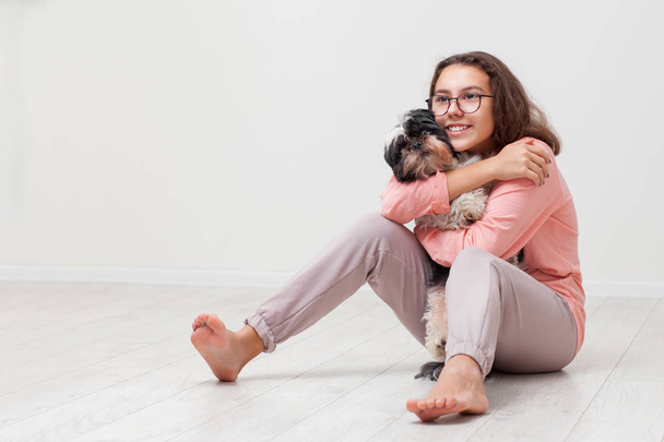 Szczęśliwa dziewczyna przytula psa. dziecko z małymi psami bawiącymi się w domu. Nastolatek ze szczeniakiem siedzi na podłodze na białym tle. - Zdjęcie, obraz