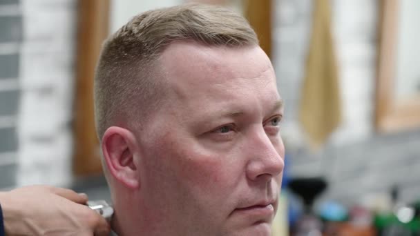 Mens haircut in Barbershop. Close-up of master clipping a man with blond hair with clipper - Imágenes, Vídeo