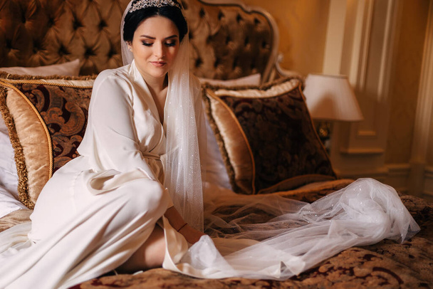 novia en túnica blanca con velo de boda sentado en la cama en el
  - Foto, imagen