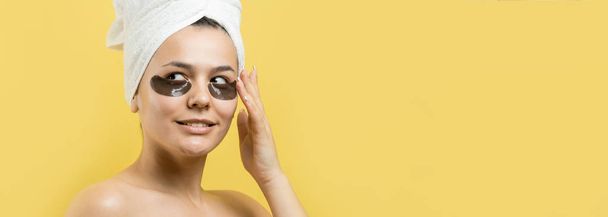 Young beautiful girl in a white towel on his head wears collagen gel patches under her eyes. Mask under eyes treatment face. - Photo, Image