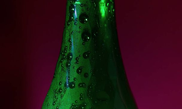 drops of water on the green bottle of beer on red blurred background - Photo, Image