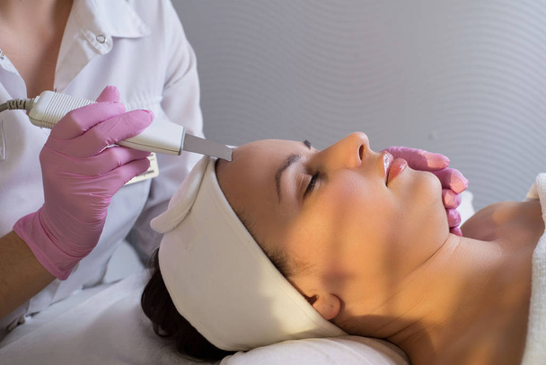 zbliżenie, profesjonalny kosmetyczka za pomocą ultradźwiękowego środka do czyszczenia twarzy, oczyszcza skórę pacjenta dziewczyny, w salonie piękności - Zdjęcie, obraz