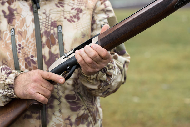Carga un rifle de caza de calibre liso, cazando un faisán con perros. Un cazador en camuflaje está de pie con un arma
. - Foto, Imagen