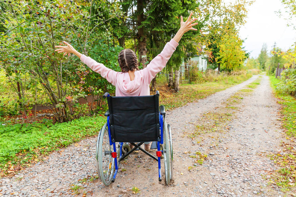 Jeune femme handicapée heureuse en fauteuil roulant sur la route dans le parc de l'hôpital jouissant de la liberté. Fille paralysée dans une chaise invalide pour les personnes handicapées en plein air dans la nature. Concept de réhabilitation. - Photo, image