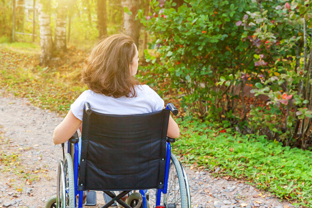 Jonge vrolijke gehandicapte vrouw in rolstoel op de weg in ziekenhuispark geniet van vrijheid. Verlamd meisje in ongeldige stoel voor gehandicapten buiten in de natuur. Revalidatieconcept. - Foto, afbeelding