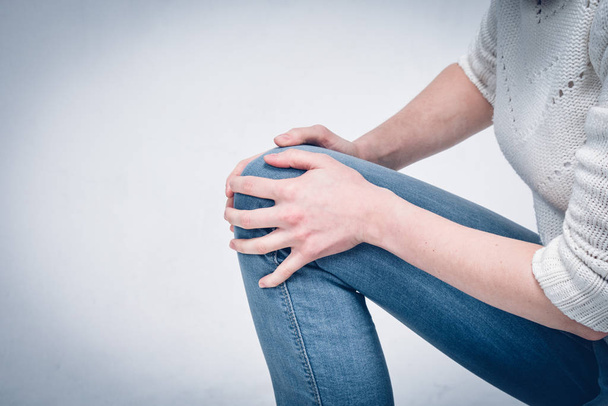 Una chica en un suéter blanco y jeans masajea su rodilla después de un fuerte moretón en el suelo
. - Foto, imagen