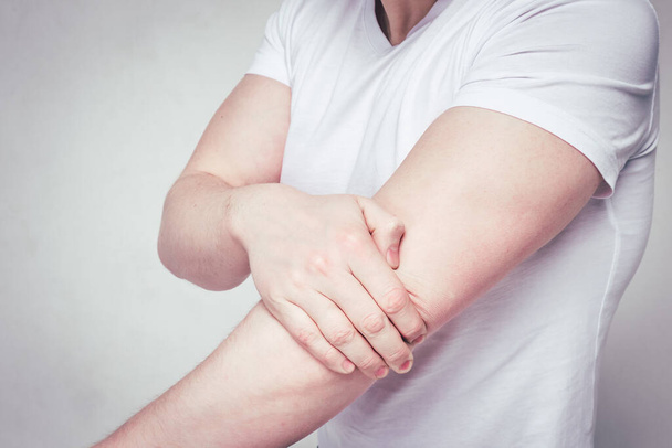 Un hombre con una camiseta blanca sufre de dolor después del gimnasio en la articulación del codo. Tonificado
. - Foto, imagen