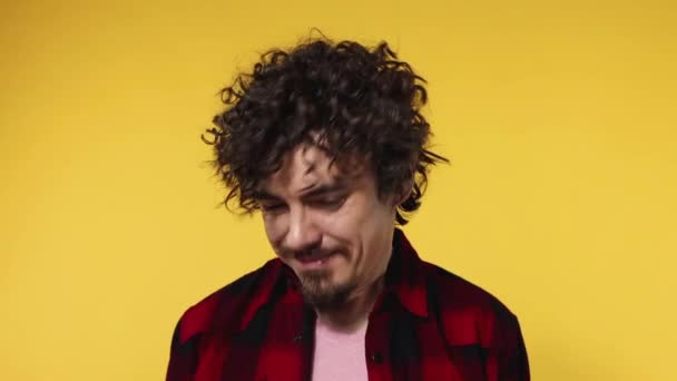 Handsome happy european man with curly hair shakes his head. Guy with beard and mustache in red shirt smiling and dancing isolated on yellow background. Lifestyle concept. Slow motion. - 映像、動画