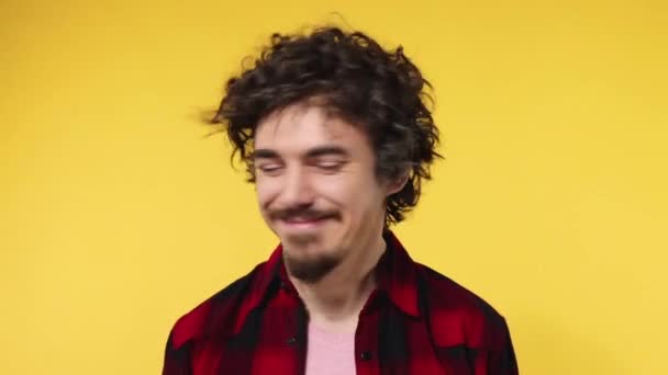 Handsome happy european man with curly hair shakes his head. Guy with beard and mustache in red shirt smiling and dancing isolated on yellow background. Lifestyle concept. Slow motion. - Metraje, vídeo
