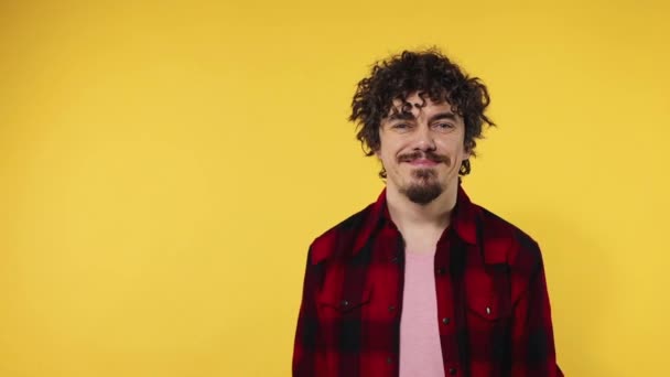 Man shows ok sign with fingers. Closeup portrait of happy smiling guy with curly hair looking at camera isolated on yellow background. Slow motion. - Video