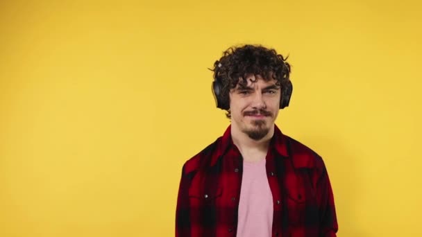 Handsome happy european man with beard in red shirt smiling and dancing isolated on yellow background. Guy in headphones listening to music. Lifestyle concept. Slow motion. - Séquence, vidéo