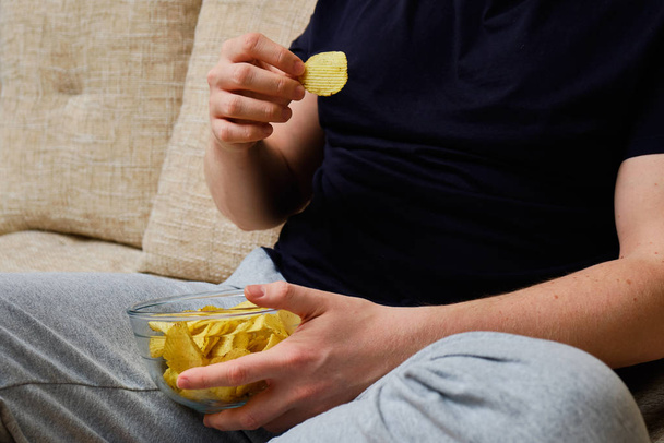 A man sitting on a sofa eating chips from a glass dish - Φωτογραφία, εικόνα