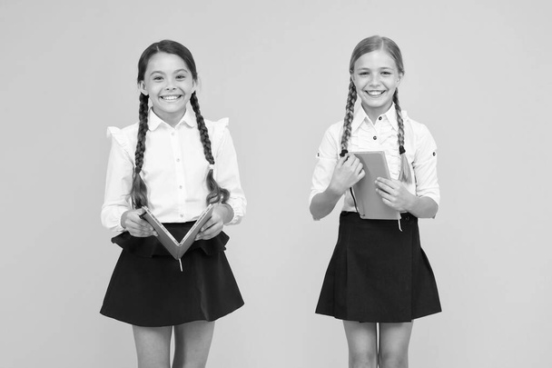 Schoolgirls study together on yellow background. Study language. Cute children study with textbook. Practice and improve reading skills for school studies. Back to school concept. Girls hold book - Photo, Image
