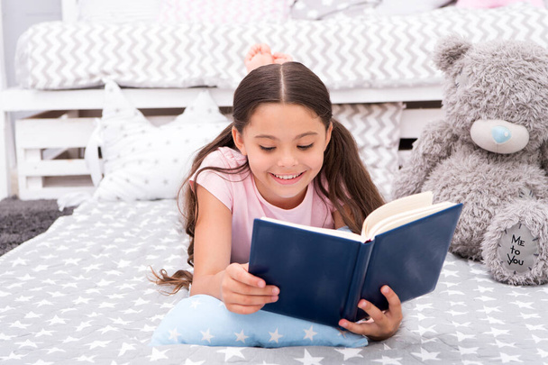 Book about love. Favorite fairy tale. Once upon a time. Girl child in bed read book with teddy bear plush toy. Pleasant time in cozy bedroom. Girl kid long hair cute pajamas relax and read book - Φωτογραφία, εικόνα