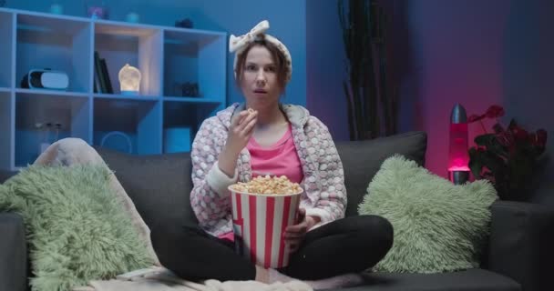 Cheerful casual woman with funny face eating popcorn and looking film sit on sofa enjoy sincere positive emotions screaming with laughter concept - Imágenes, Vídeo