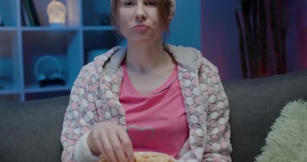 Young lady is watching TV laughing and eating popcorn having fun at home alone enjoying modern television. Youth lifestyle and cheerful people concept - Кадры, видео