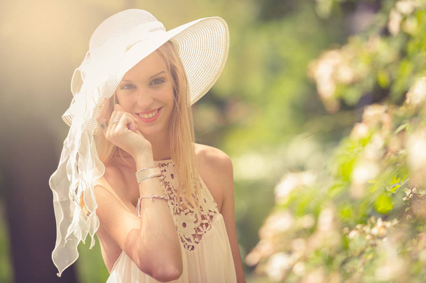 Nahaufnahme einer blonden Frau mit weißem Hut, die auf einen blühenden Baum blickt - Foto, Bild