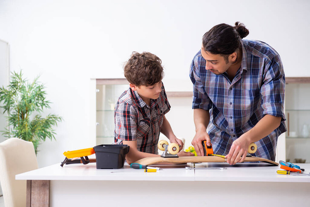 Young father repairing skateboard with his son at home - Photo, Image
