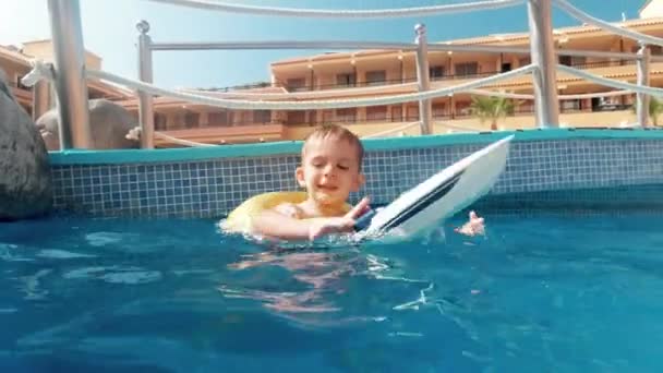 4kビデオの幸せな笑顔小さな男の子プールでプールともにインフレータブルリングと遊びますおもちゃのボート - 映像、動画