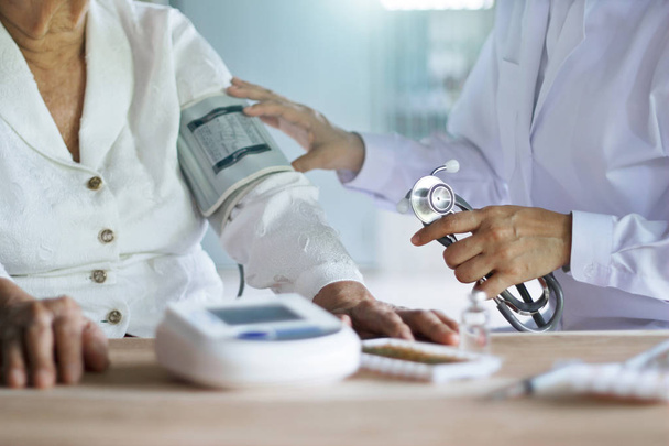 Ärztin mit Stethoskop, die sich um ältere Patientinnen im Krankenhaus kümmert und ihr Blut kontrolliert. - Foto, Bild