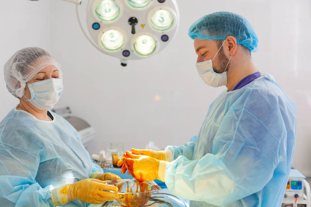 Hospital. Surgeon operates in the operating room. The doctor and nurse disinfect the implant before inserting it during breast augmentation surgery. - Foto, afbeelding