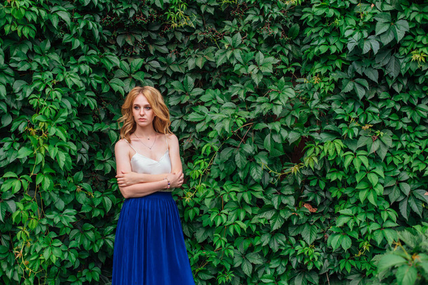 Portrait of a young beautiful woman, standing next to the wall of wild grape leaves. - Foto, afbeelding