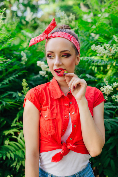 Beautiful young pin up girl with bright make up eating fresh natural strawberry. - Photo, image