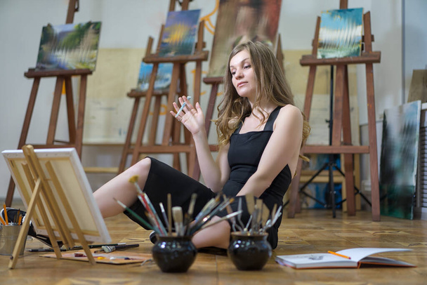 Retrato de una artista sentada en el suelo y pintando en el estudio de arte
. - Foto, Imagen