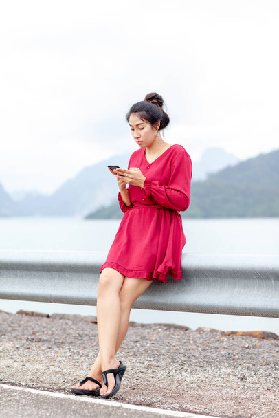 Korkulukta oturan ve akıllı telefon kullanan genç Asyalı kadın. - Fotoğraf, Görsel