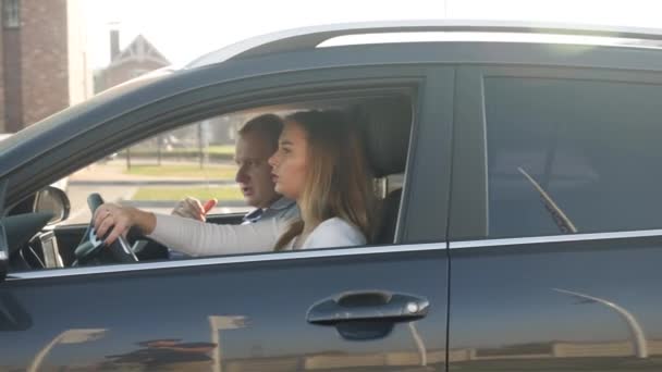 4k wideo instruktora jazdy mężczyzna siedzi na siedzeniu pasażera w samochodzie i pokazuje drogę do uczennicy w szkole jazdy - Materiał filmowy, wideo
