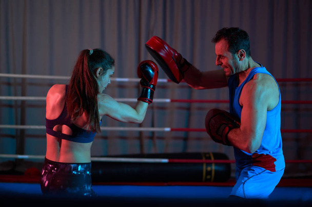 Female kickboxer hitting mitts with her coach in the ring - Foto, afbeelding