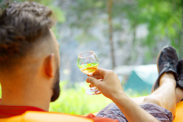 a man against the background of nature drinks from a glass while lying on an air mattress on a sunny summer day - Foto, Imagen