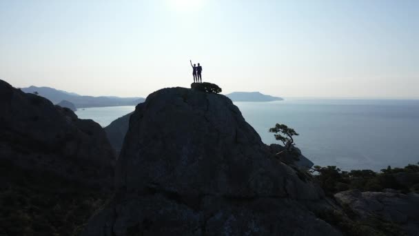Een paar jonge mensen beklommen een hoge berg, genietend van de prachtige horizon van de Zwarte Zee en de lucht. Twee jonge toeristen veroverd berg, bovenaanzicht van opzij. - Video