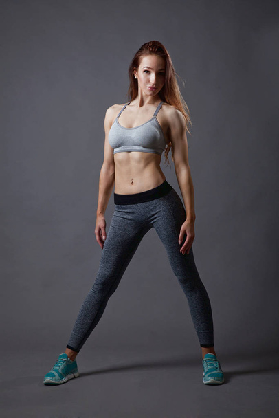 athletic young girl, fitness trainer, posing in modern clothes on a gray background - Valokuva, kuva